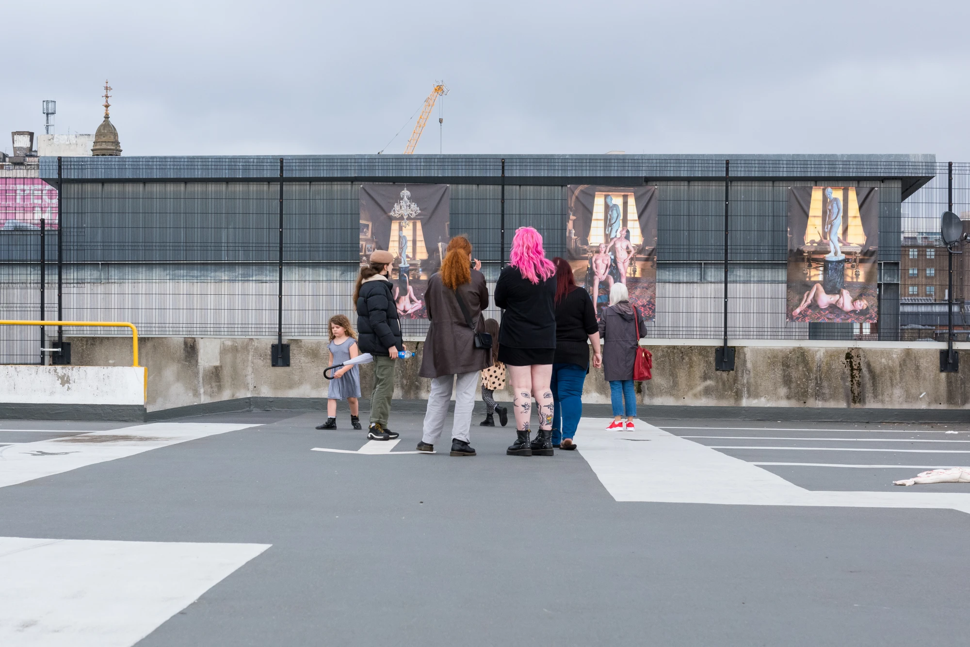 people looking at prints hung in a car park.