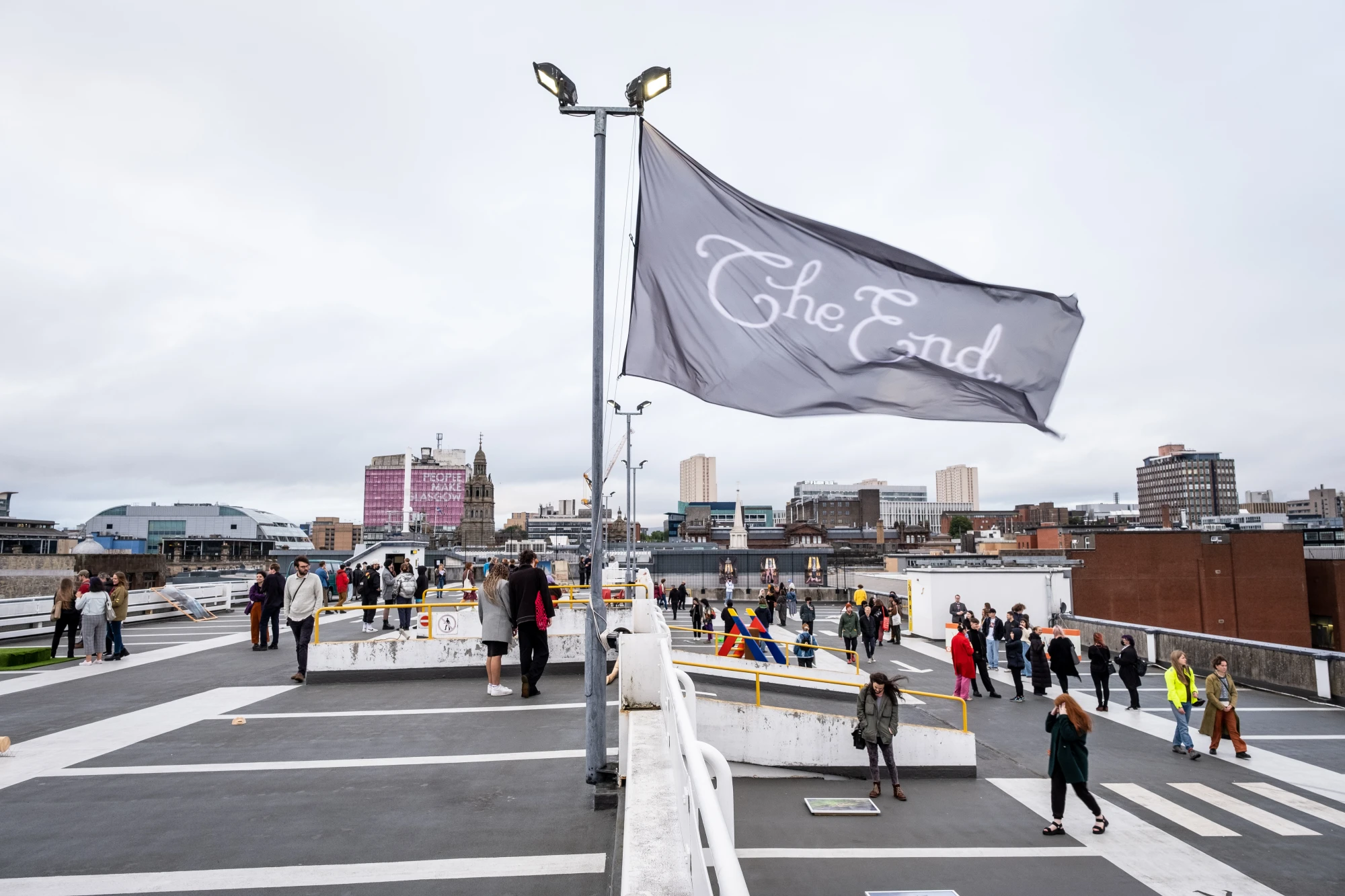 a giant flag featuring the text 'the end' flys over the roof of a multi storey car park that functions as a gallery space