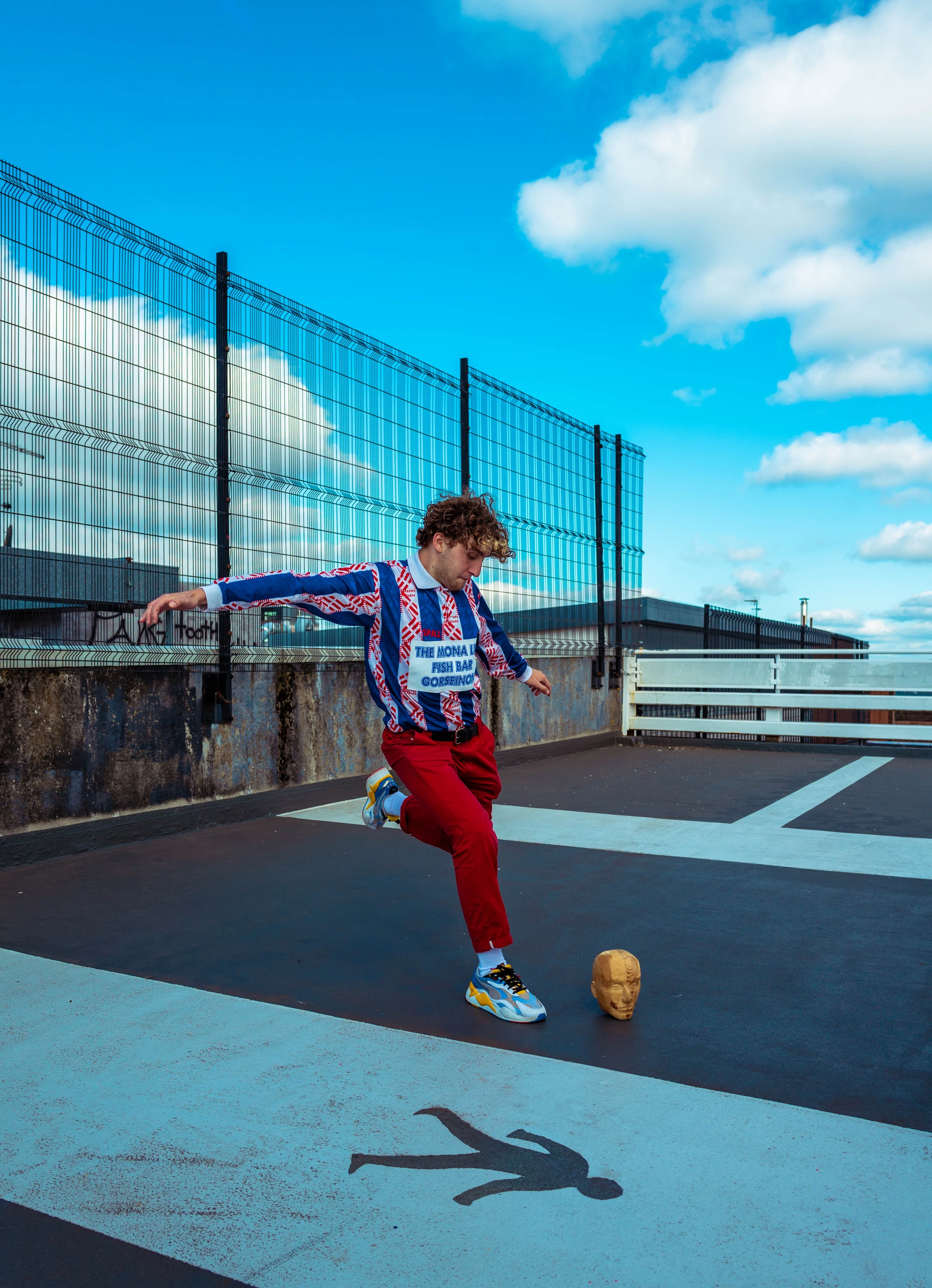 a man wearing a stripey top and red trousers kick a wooden skull like a football.