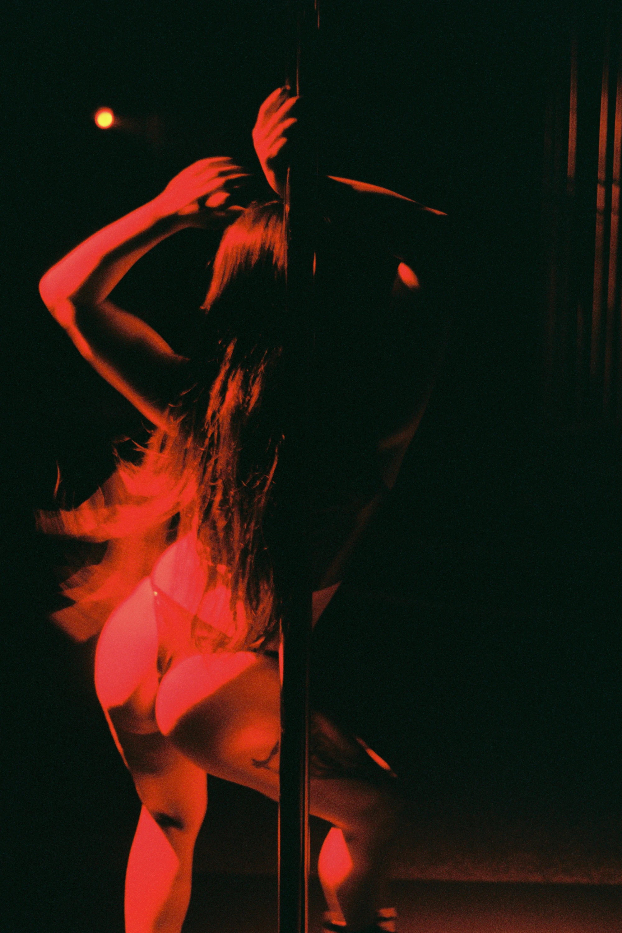 a woman moves around a pole under a red light.