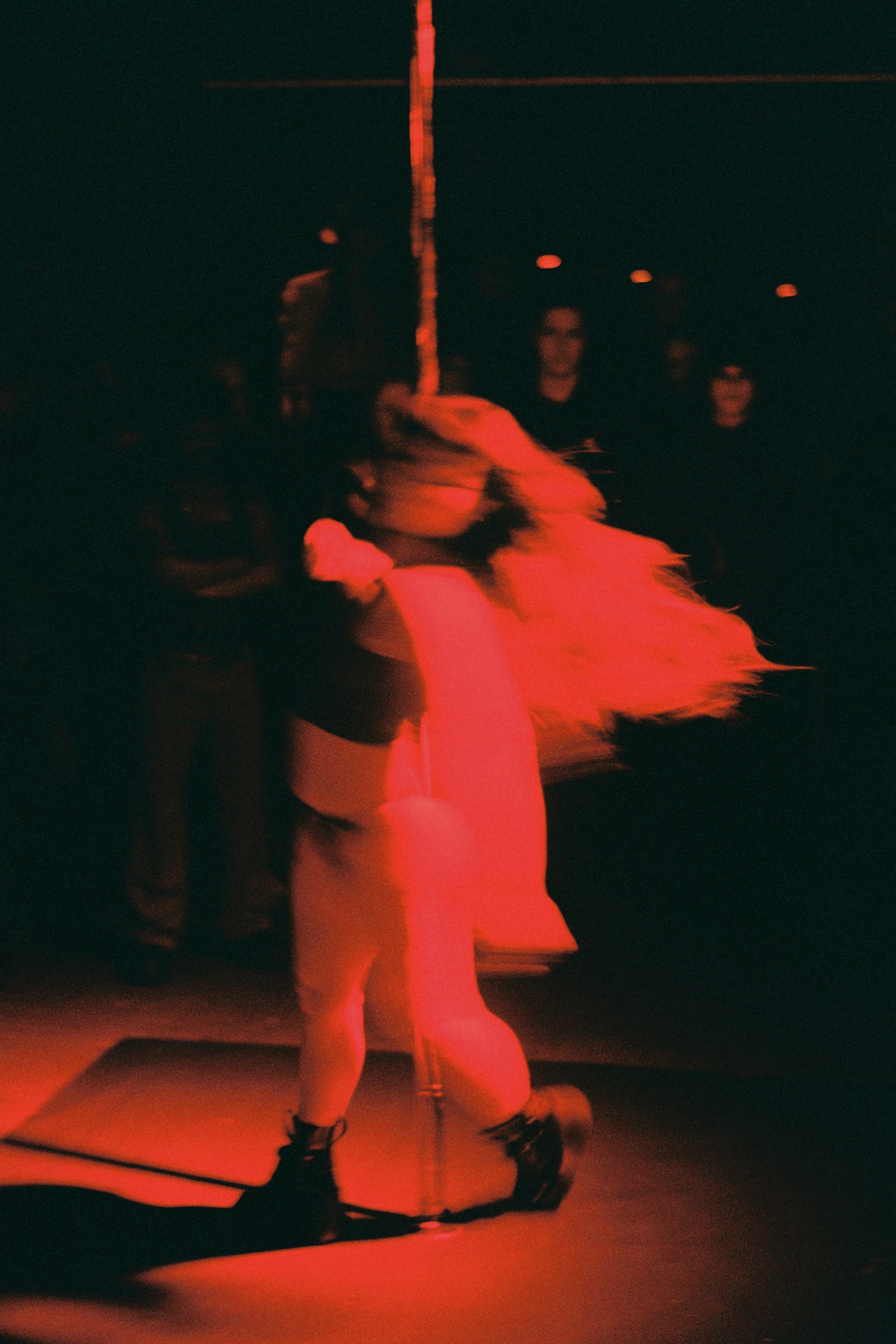 a woman moves around the pole under a red light.