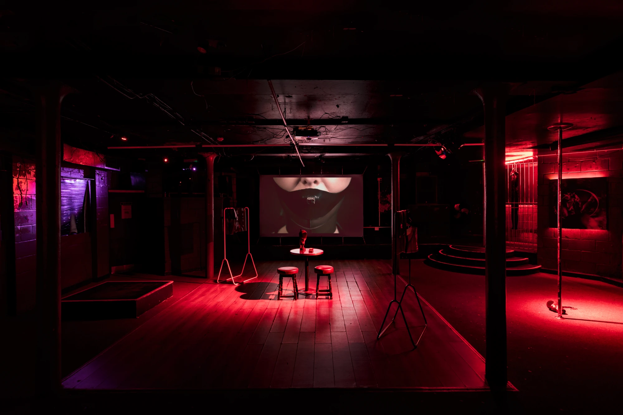 a dark red space showing a projection screen at the back, and a table with two stools at the front.