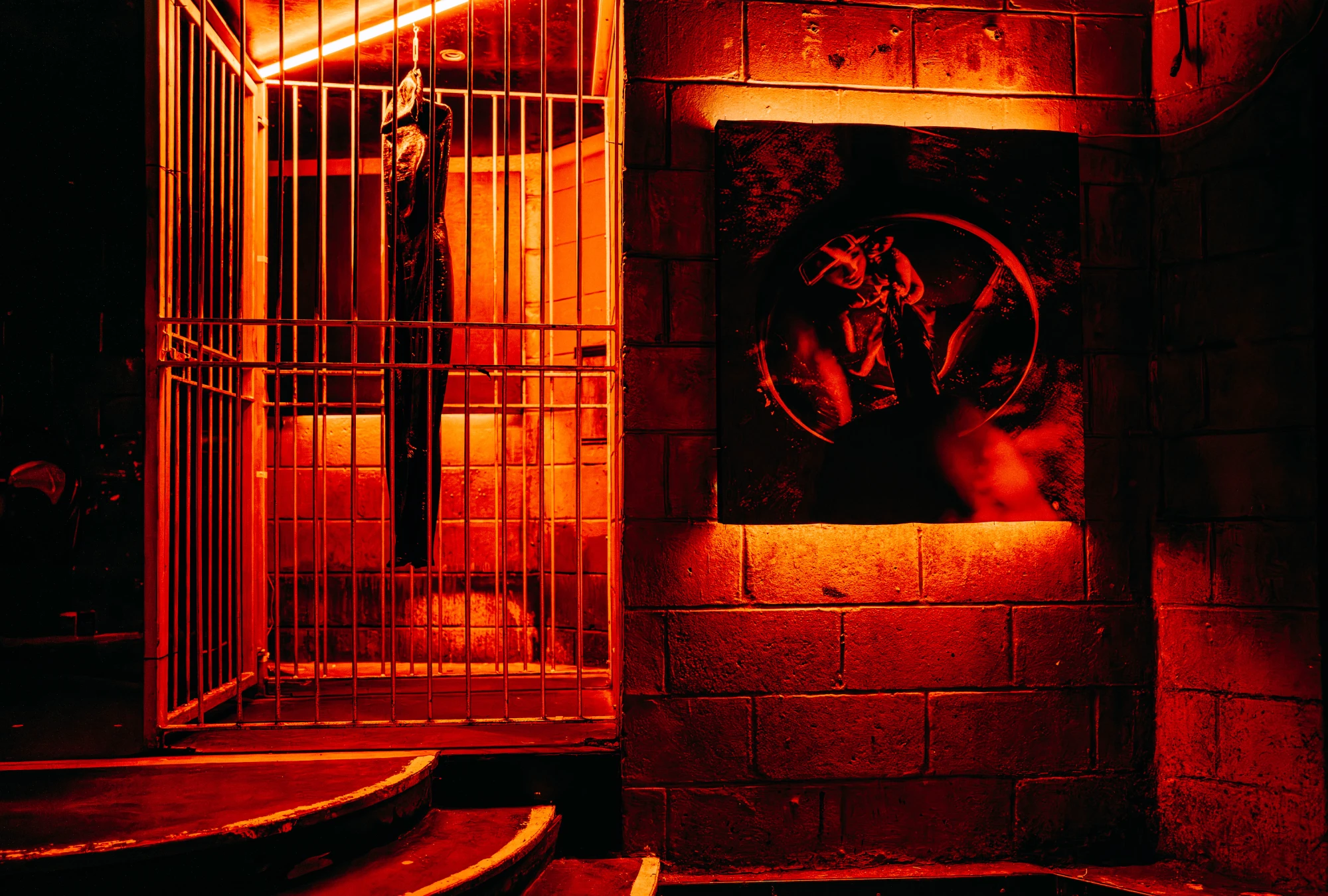 a dark red space featuring a latex dress hanging in a cage and a print mounted on a wall next to it.