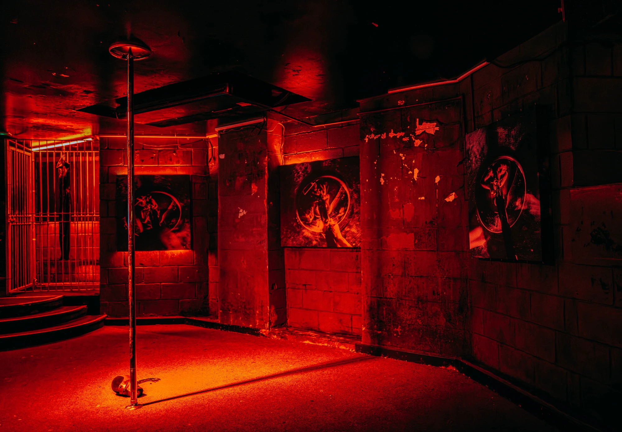 a dark red industrial space featuring a latex dress hanging in a cage and three prints on the walls.
