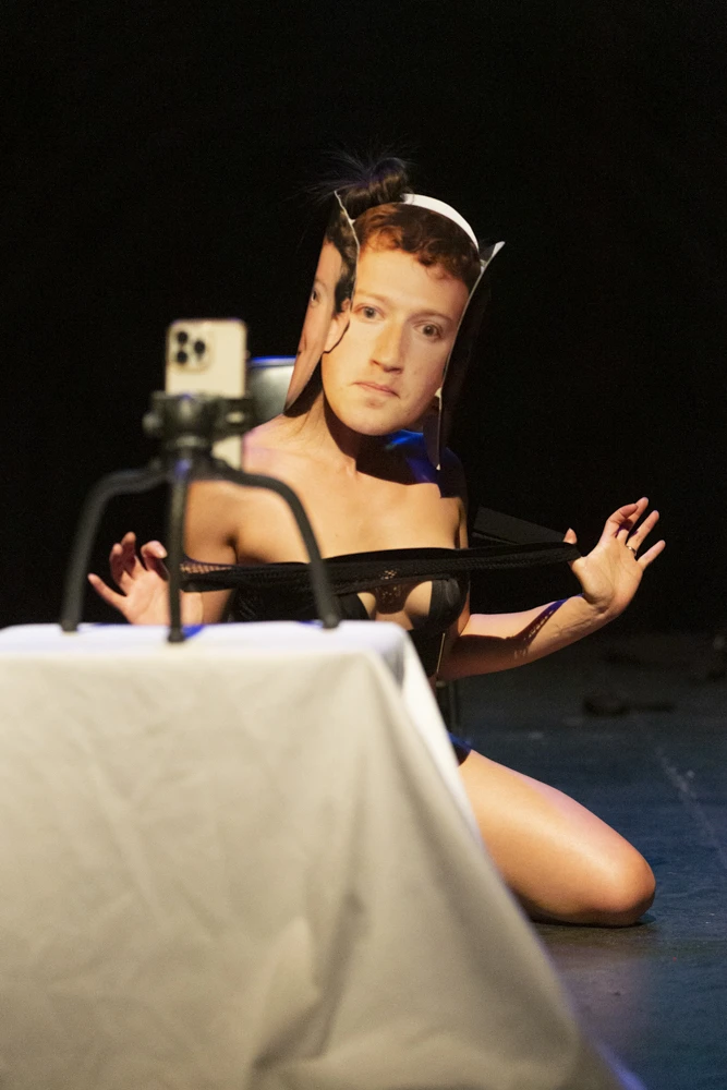 a woman wearing black hoodie and sweatpants performs as Mark Zuckerberg.