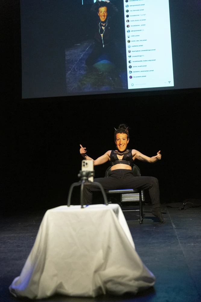 a woman wearing black hoodie and sweatpants performs as Mark Zuckerberg.