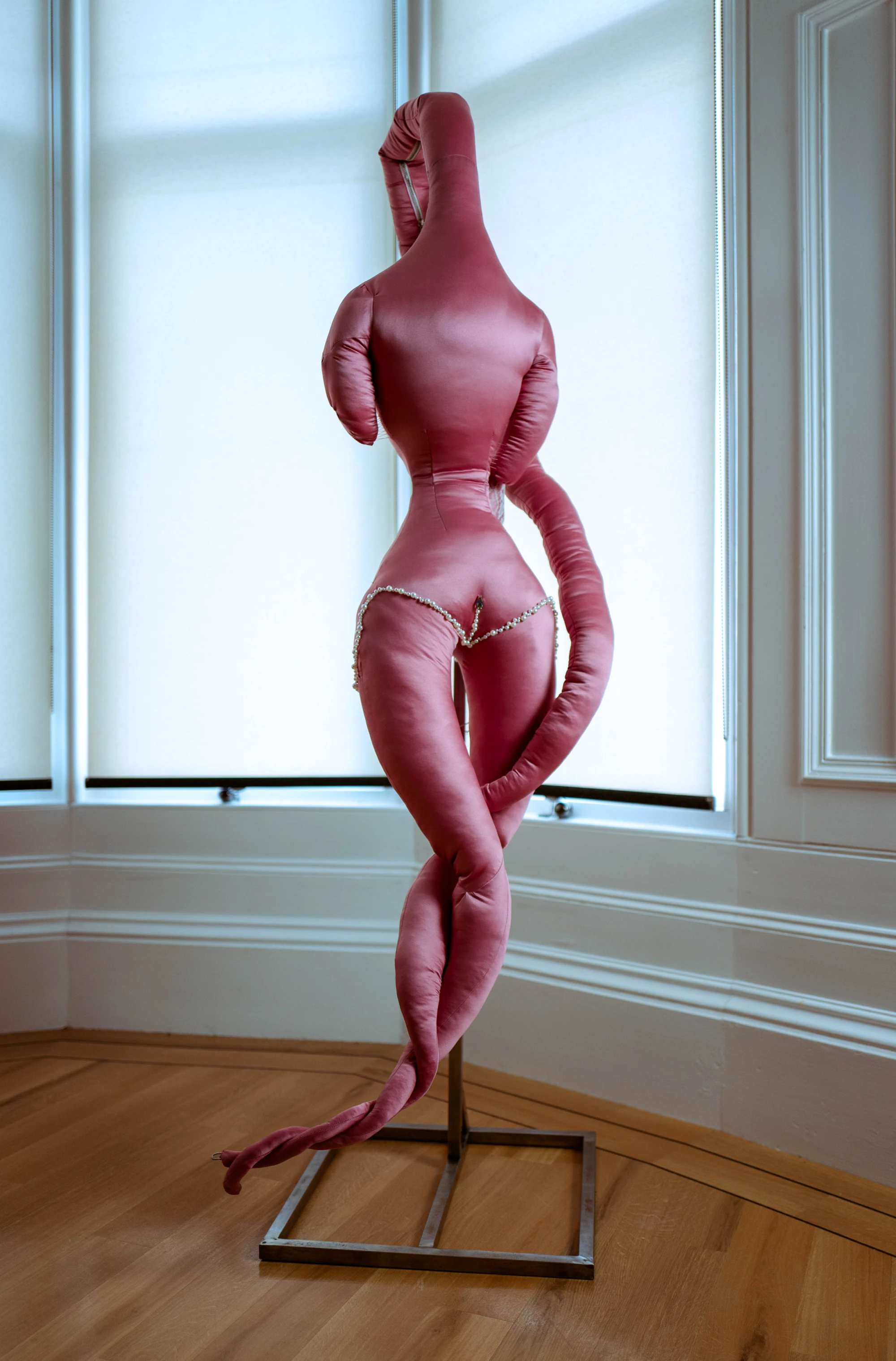 a satin pink soft scultpure hangs on a steel stand.