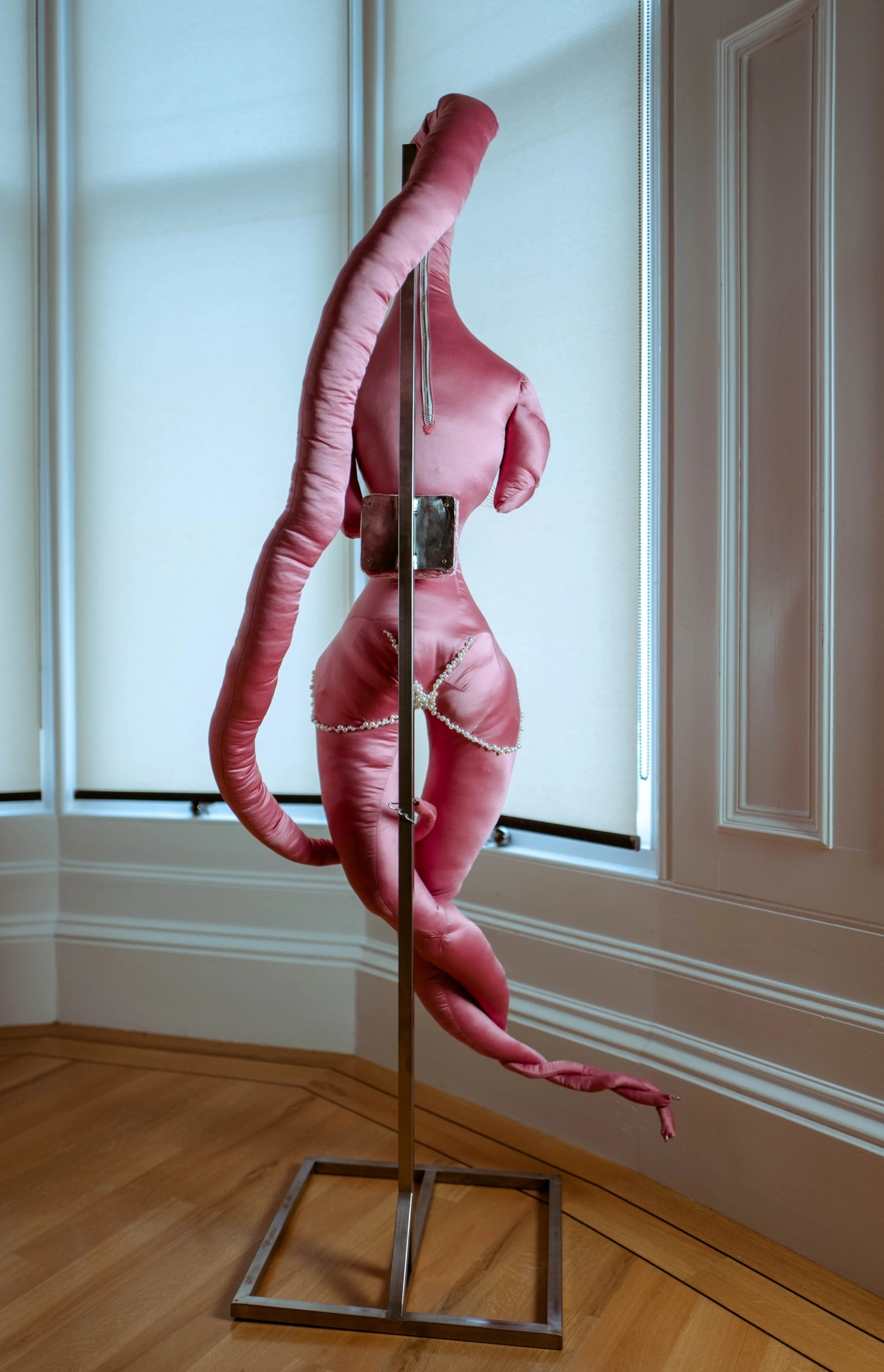 a satin pink soft scultpure hangs on a steel stand.