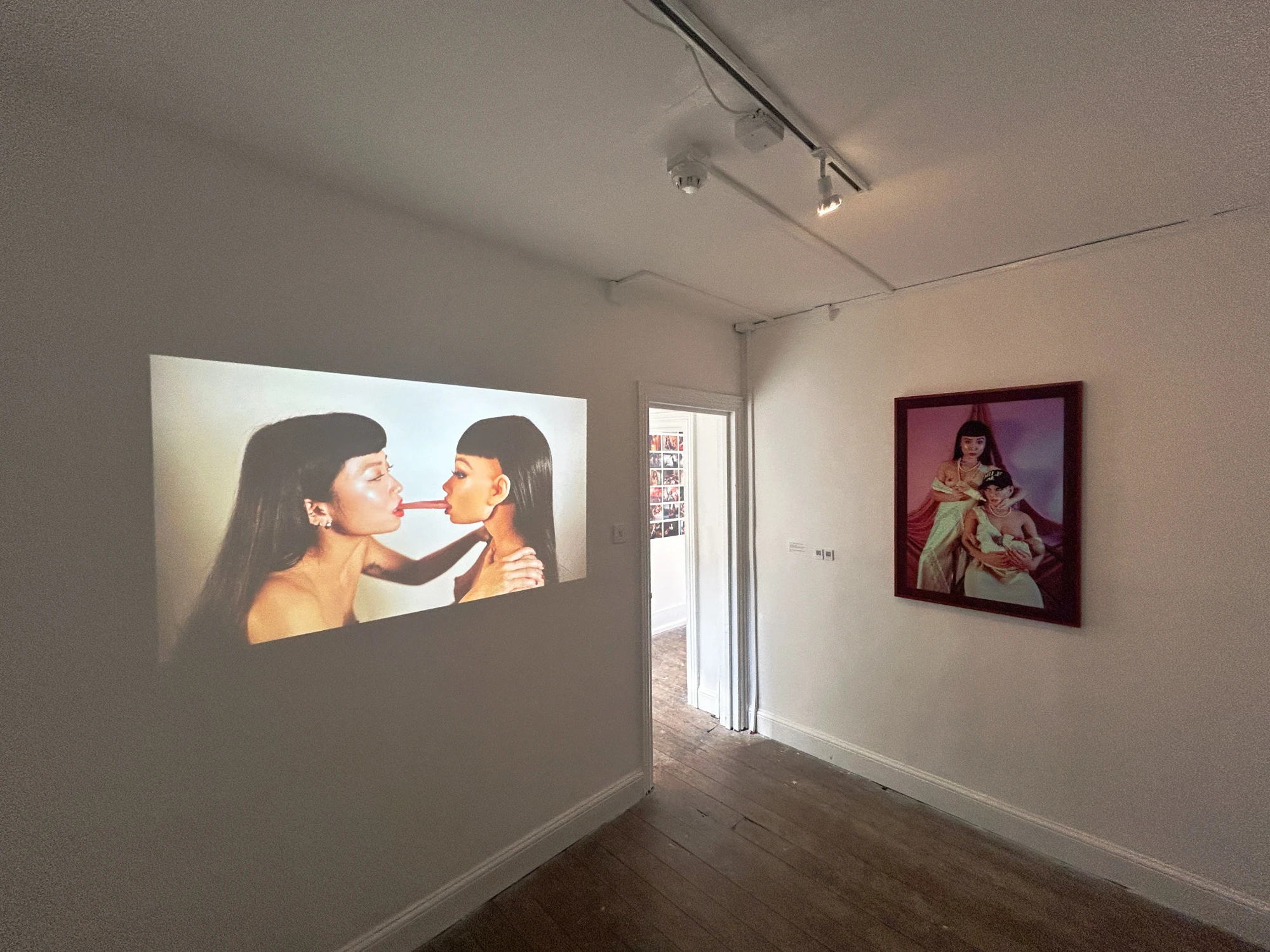 Installation view of Narratives & Counter Narratives in a darkened room, next to a photographic print of two figures.